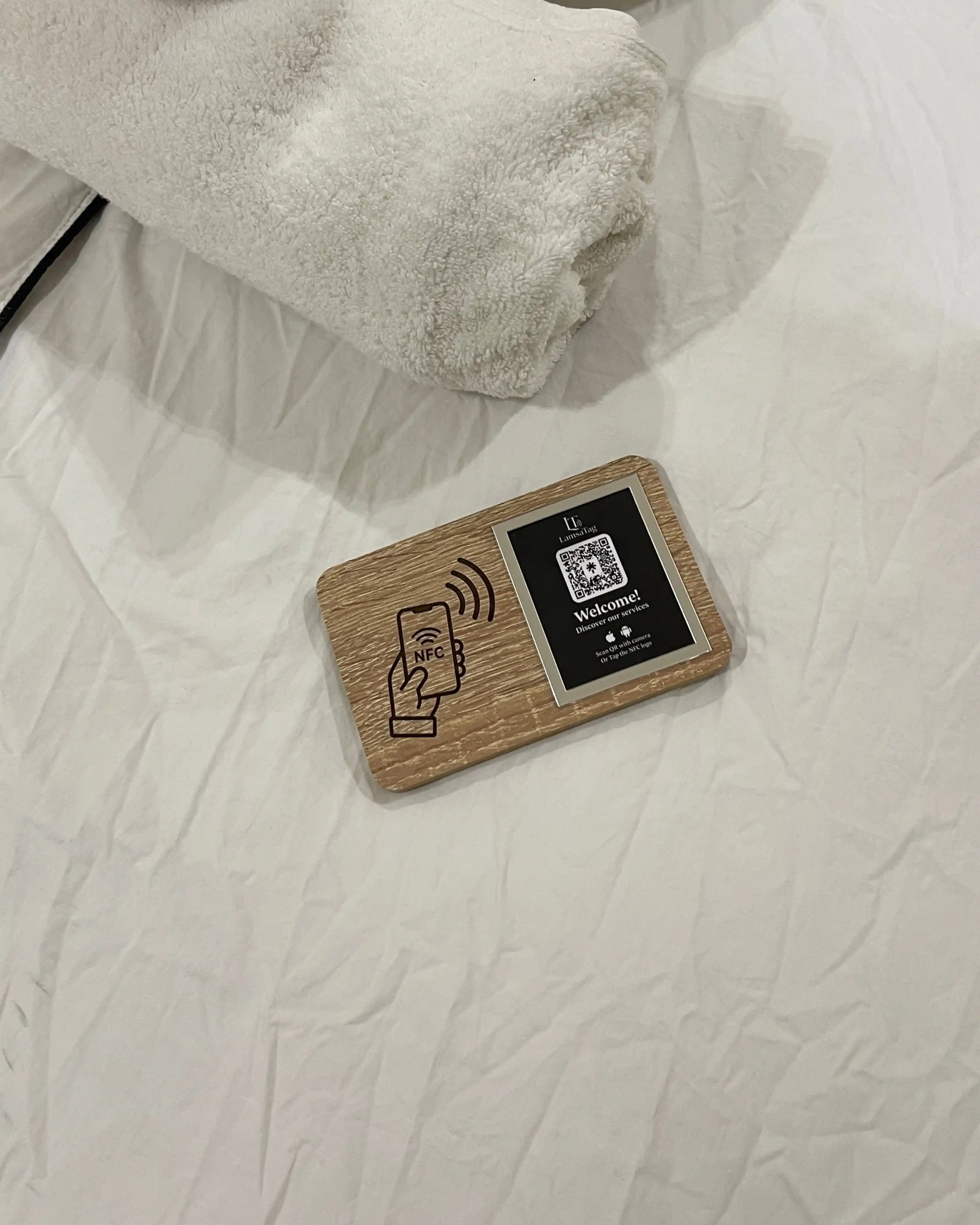 Plaque NFC LamsaTag posée sur un lit d'hôtel — conciergerie digitale au Maroc